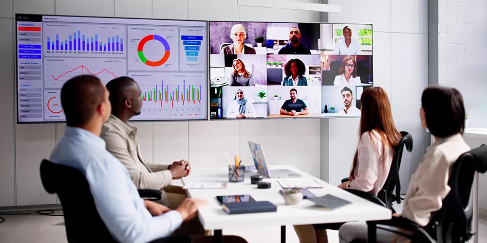 4 Personen schauen in einem Besprechungsraum auf 2 große Monitore mit Statistiken und Videokonferenzteilnehmern, Bild: iStock/AndreyPopov