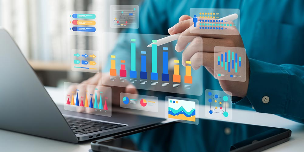 Person arbeitet an einem Laptop und einem Tablet, Diagramme schweben im Raum dazwischen, Bild. iStock/ThapanaOnphalai