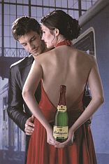 Frau und Mann stehen dicht zusammen, Frau hält Sektflasche hinter dem Rücken